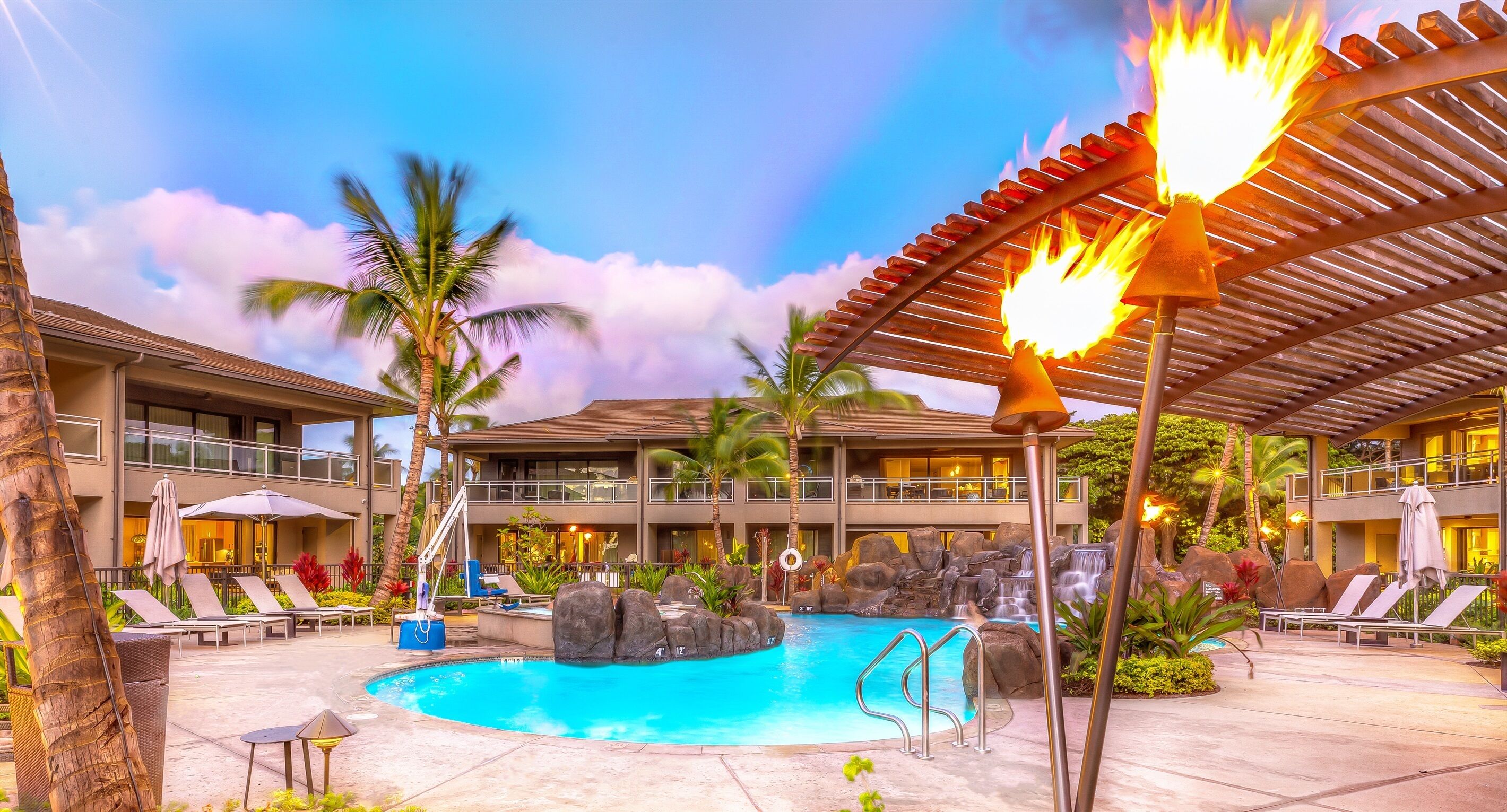 Ett poolområde på semesteranläggningen med solstolar, ett vattenfall och en bar i polynesisk stil.