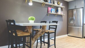 Ett modernt kök med en central köksö, trästolar, ett kylskåp i rostfritt stål och dekorativa hyllor.
