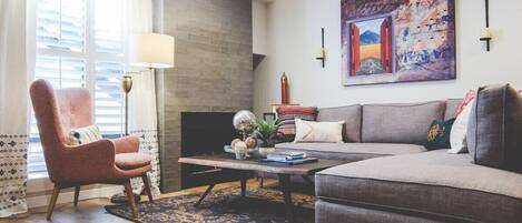 A modern living room with a sofa, armchair, coffee table, and fireplace.