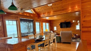 A wooden cabin interior with a dining area, kitchen, and seating space. - Designer Lake Champlain Retreat with Adirondack Views & Private Waterfront (Willsboro)