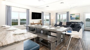 Ein modernes Wohnzimmer mit Essbereich, großen Fenstern, einem Flachbildfernseher und Blick auf das Wasser.