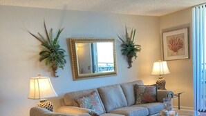 A living room with a grey sofa, two side tables with lamps, a coffee table, and decorative plants. - Hudson Hideaway: 2 BR/2 Bath Gulf Front Condo,Stunning Sunset from 27' Balcony (Hudson)