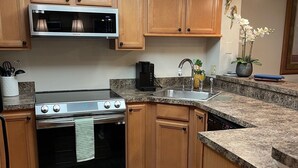 A kitchen with wooden cabinets, a stainless steel stove, a microwave, a sink, and a ceiling light. - Hudson Hideaway: 2 BR/2 Bath Gulf Front Condo,Stunning Sunset from 27' Balcony (Hudson)