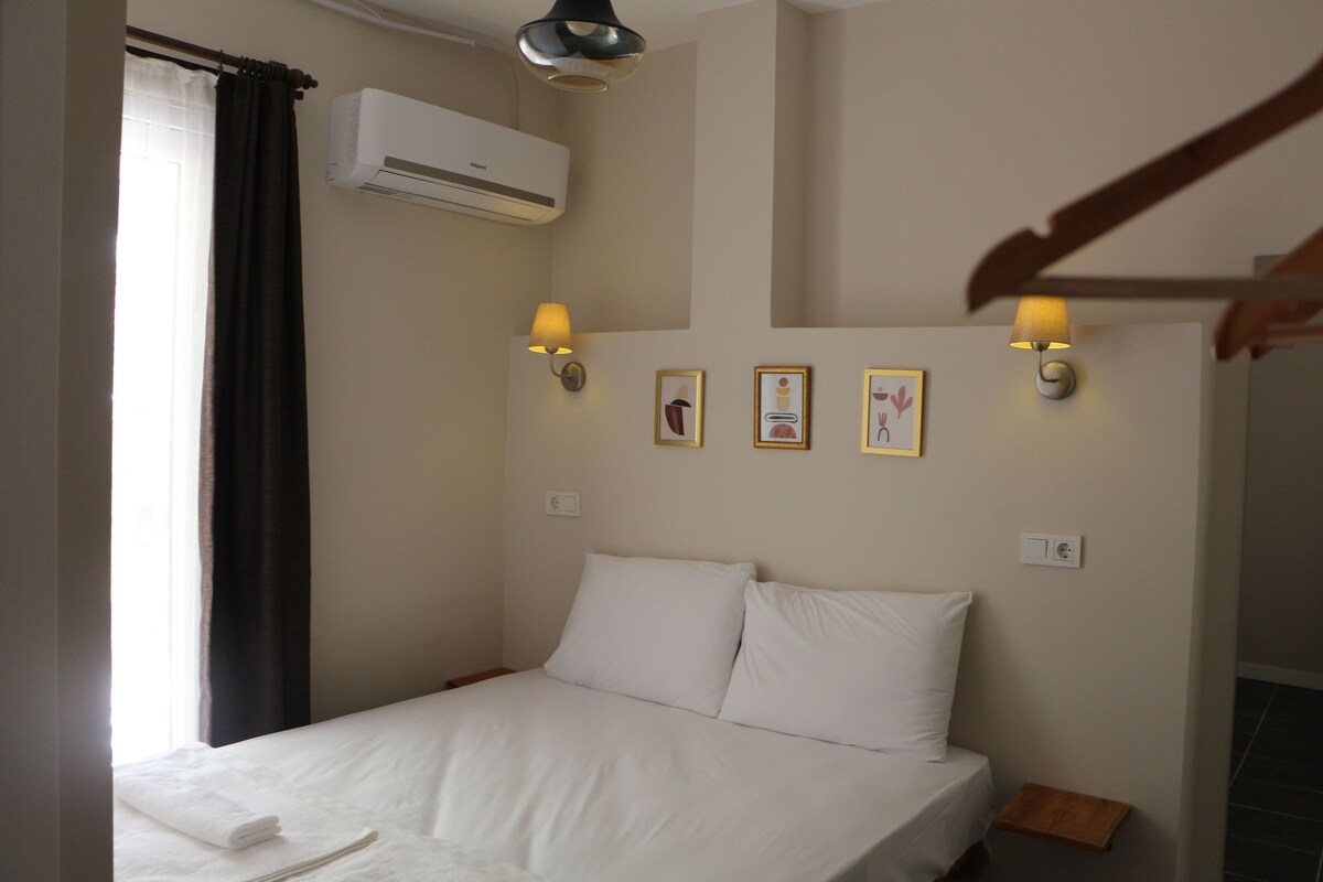 A bedroom with a bed, an air conditioning unit, wall-mounted lamps, and framed pictures on the wall.