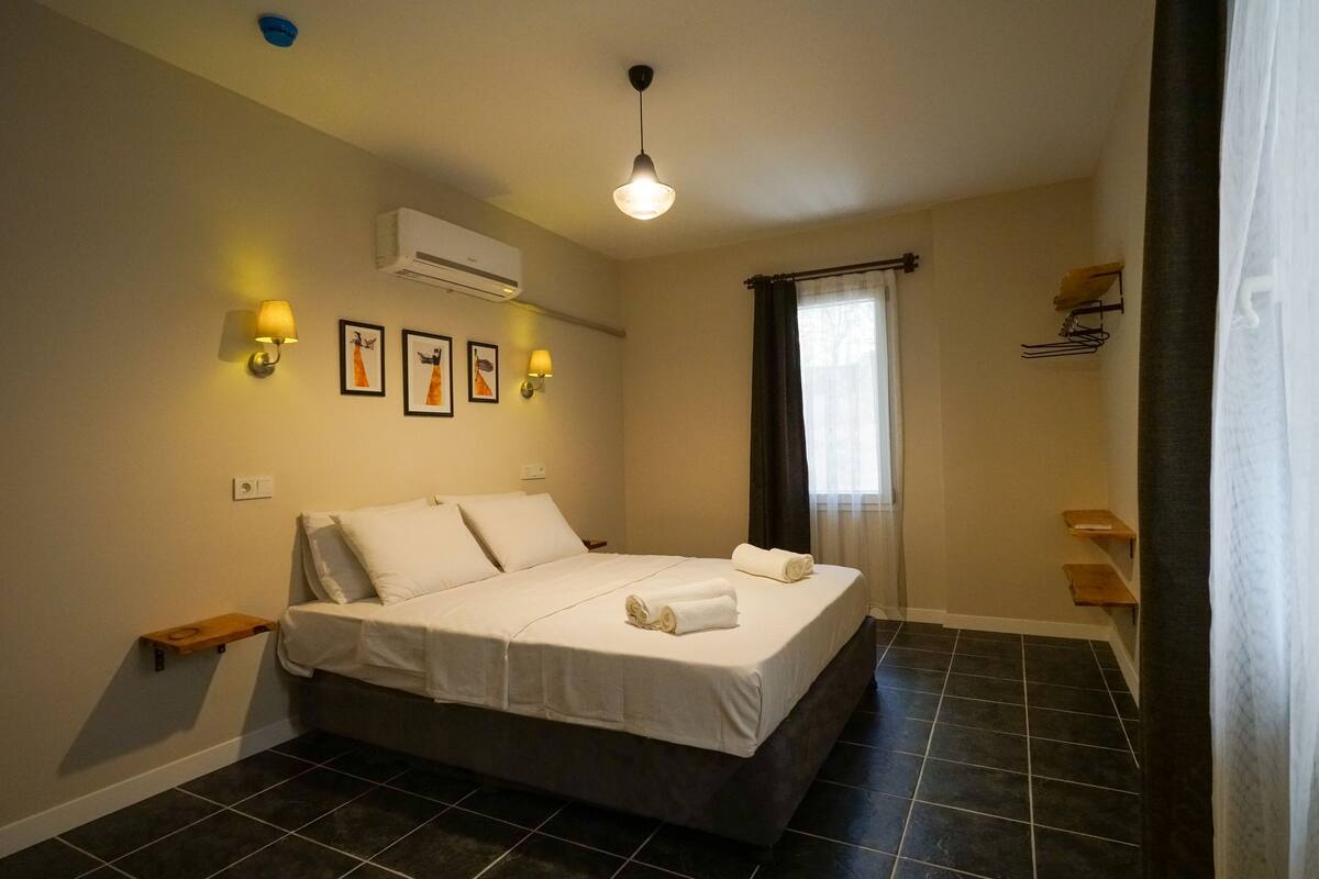 A hotel room with a large bed, two wall-mounted lamps, an air conditioner, and a window with curtains.