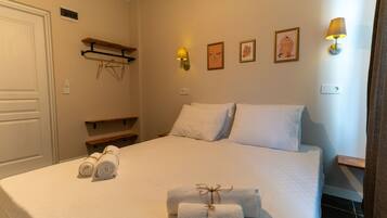 A neatly made bed with white linens, two rolled towels, and a small decorative item on the bed.