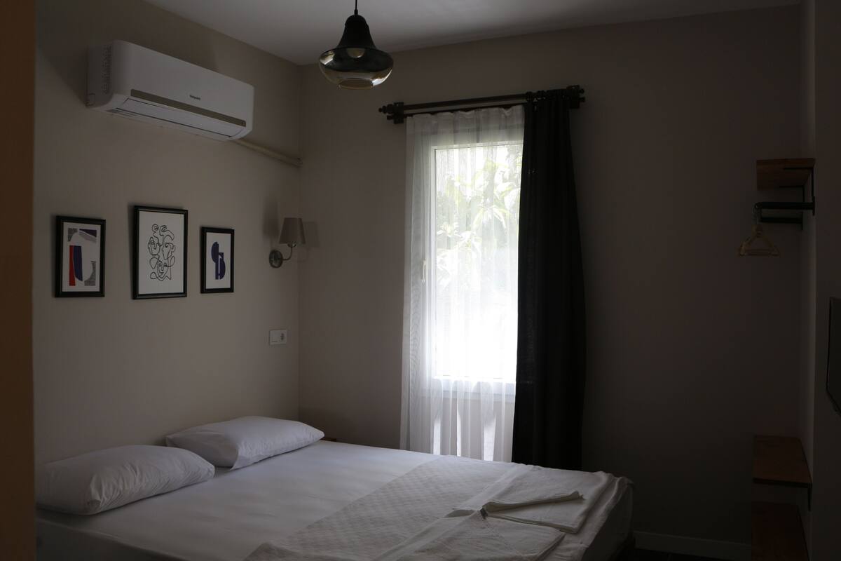 A bedroom with a bed, air conditioning unit, and three framed pictures on the wall.