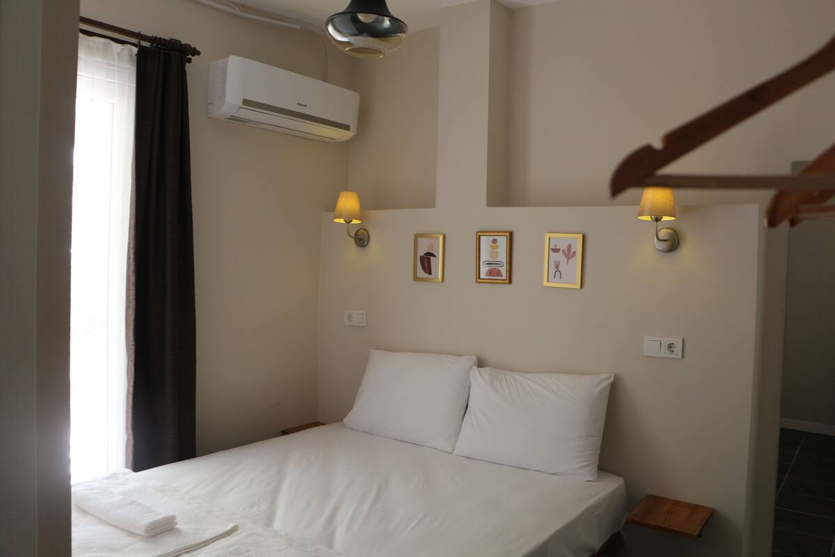 A bedroom with a bed, an air conditioning unit, wall-mounted lamps, and framed pictures on the wall.