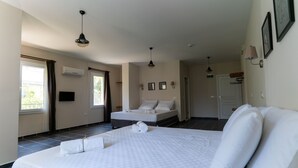 Habitación de hotel con una cama grande, una cama más pequeña, un escritorio y una silla. Hay dos ventanas y un equipo de aire acondicionado en la pared.