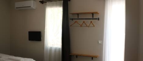 A hotel room with a bed, air conditioning unit, curtains, a TV, and wooden shelves.