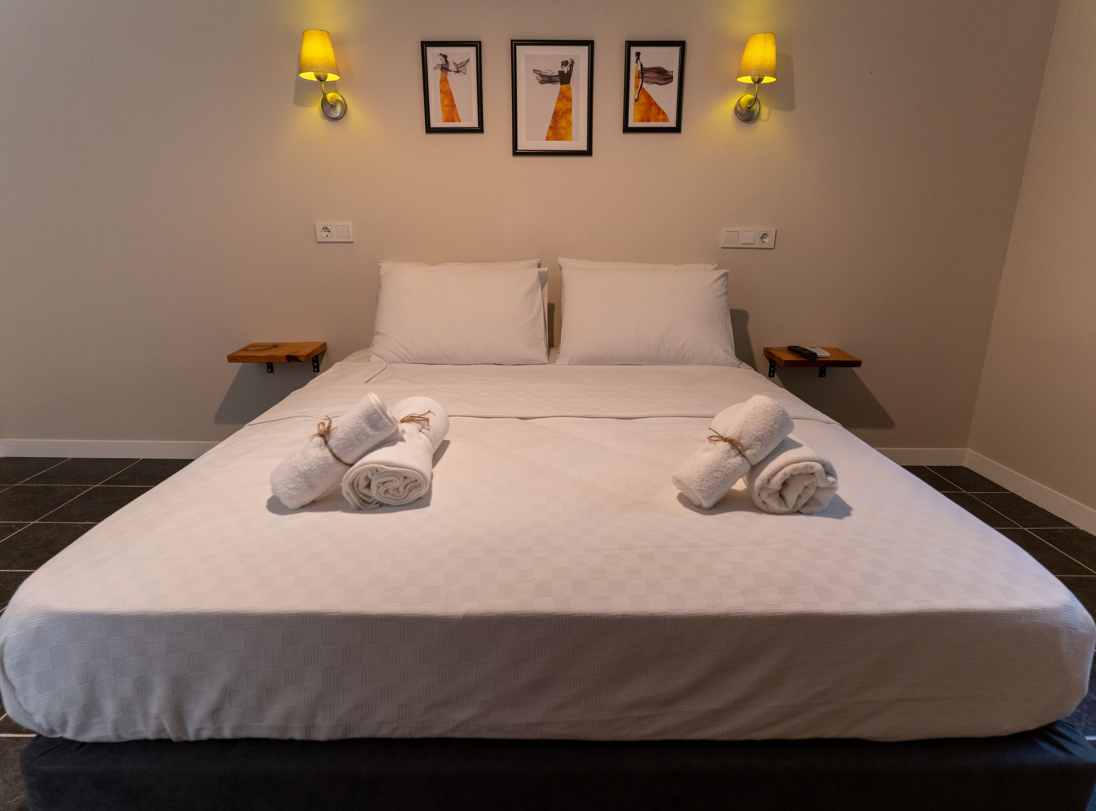 A neatly made bed with white linens, two rolled towels on the bed, and two bedside tables with lamps.