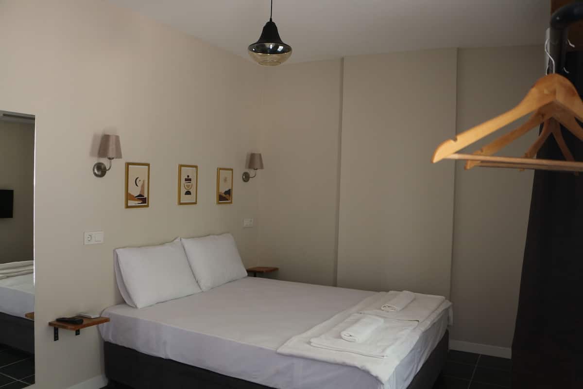 A hotel room with a bed, a wooden hanger, and wall-mounted lamps.