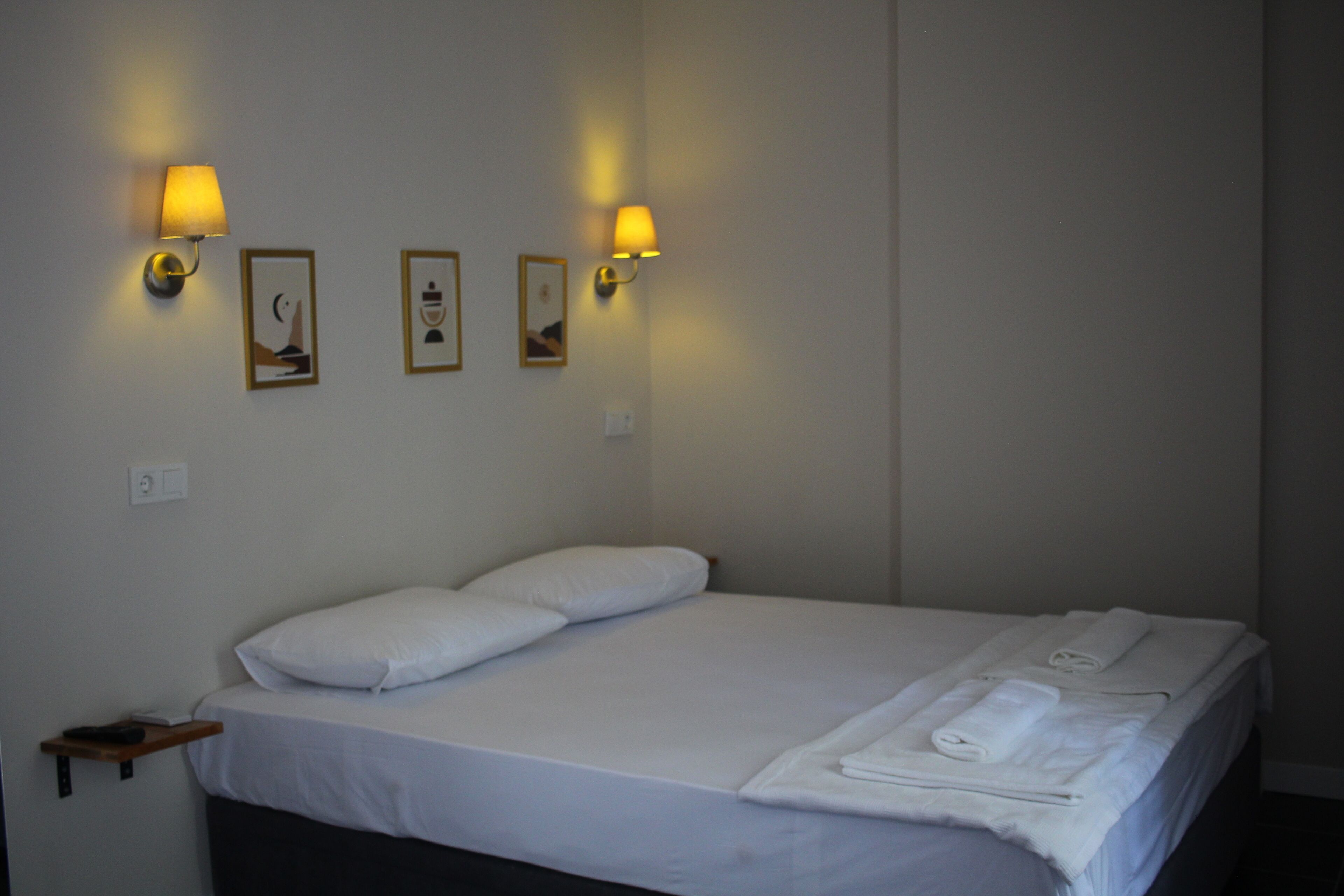 Ein Hotelzimmer mit einem Bett, weißen Laken, zwei Wandlampen und drei gerahmten Bildern an der Wand.