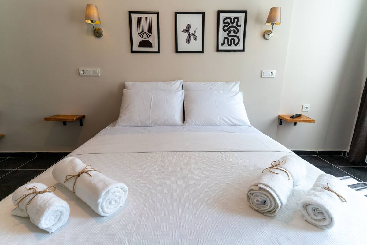 A hotel room with a large bed, white linens, two wall-mounted lamps, and three framed artworks.