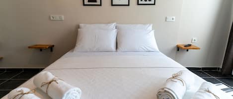A hotel room with a large bed, white linens, two wall-mounted lamps, and three framed artworks.