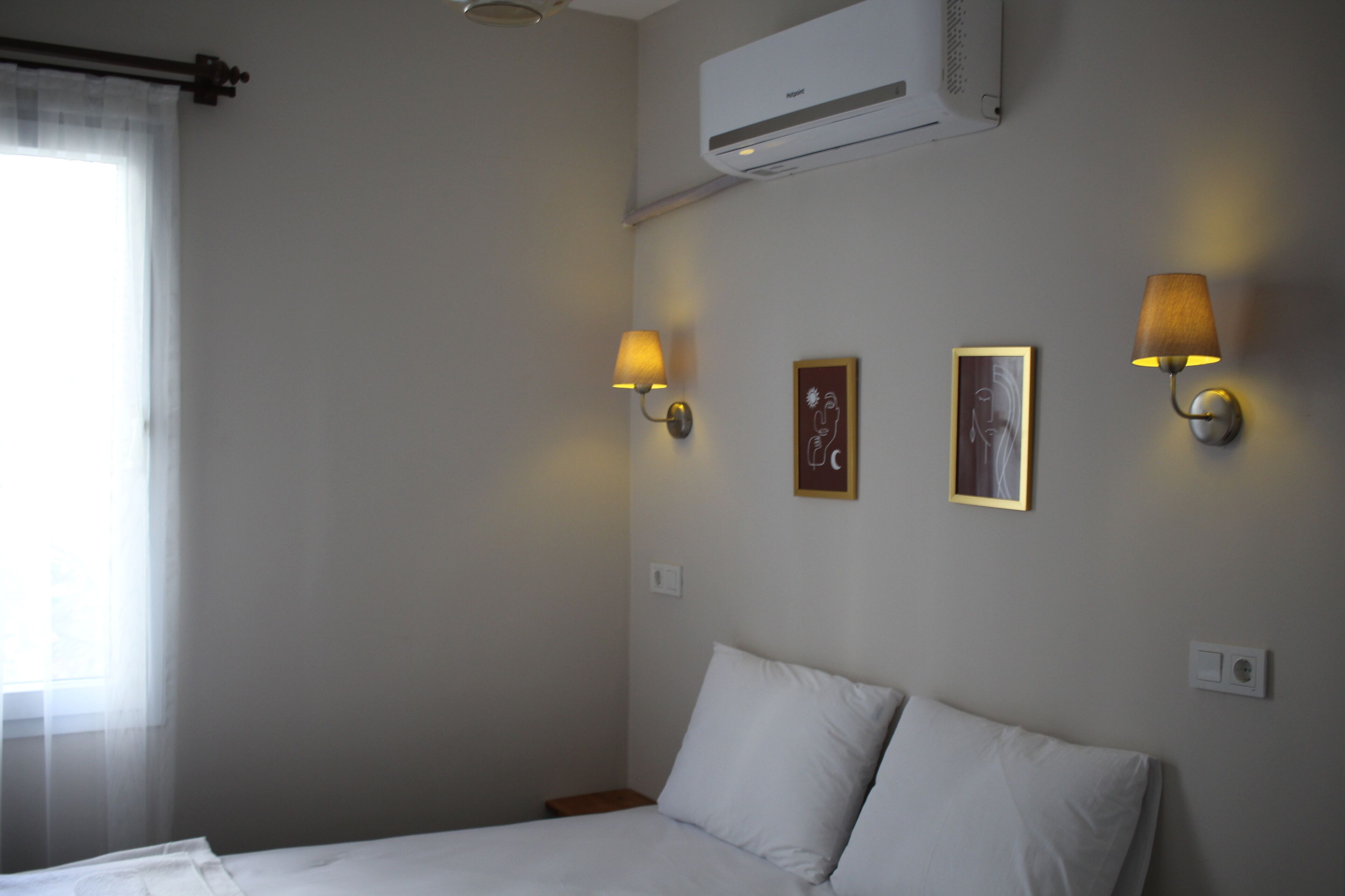 A hotel room with a bed, two wall-mounted lamps, and an air conditioning unit.