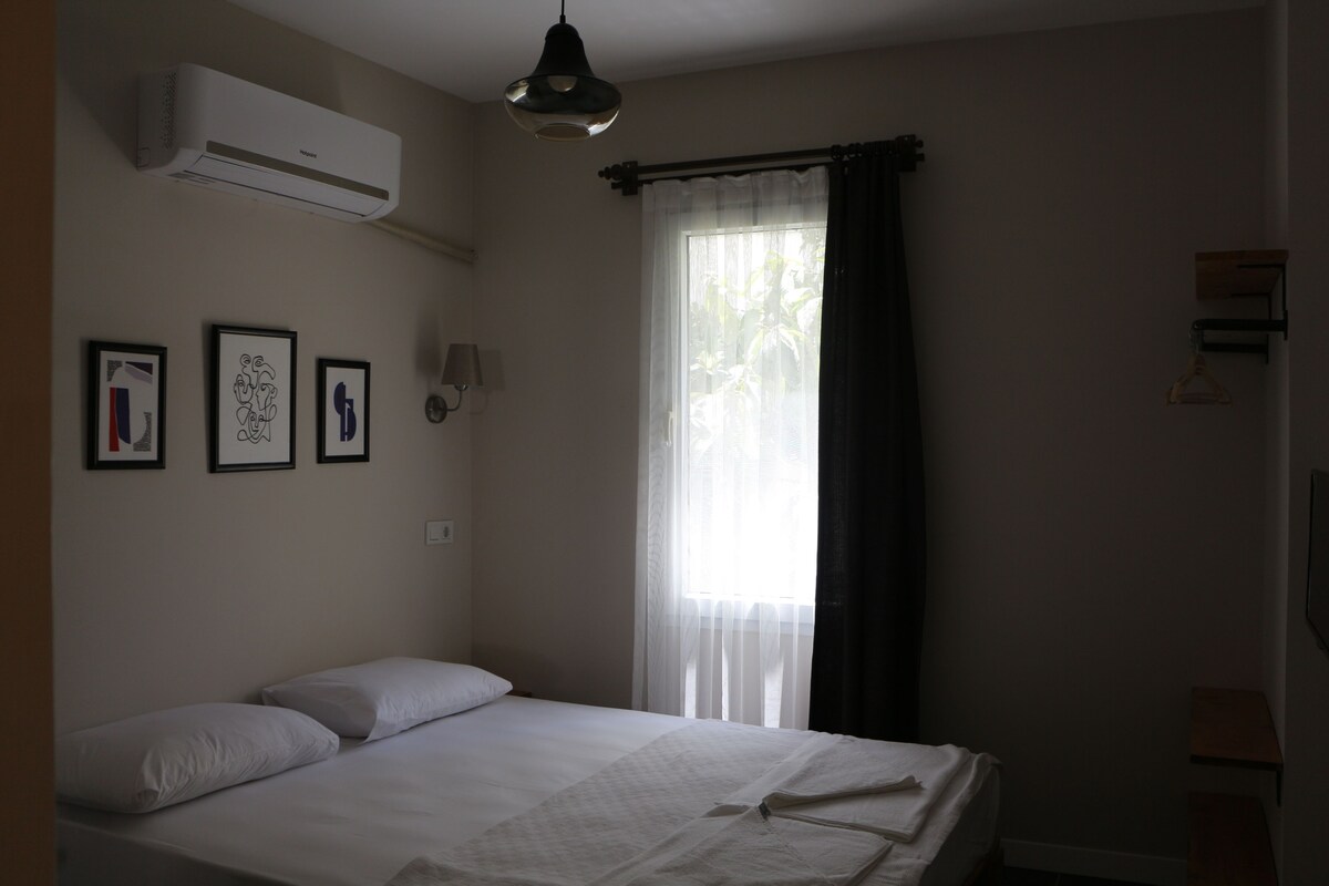 A bedroom with a bed, air conditioning unit, and three framed pictures on the wall.