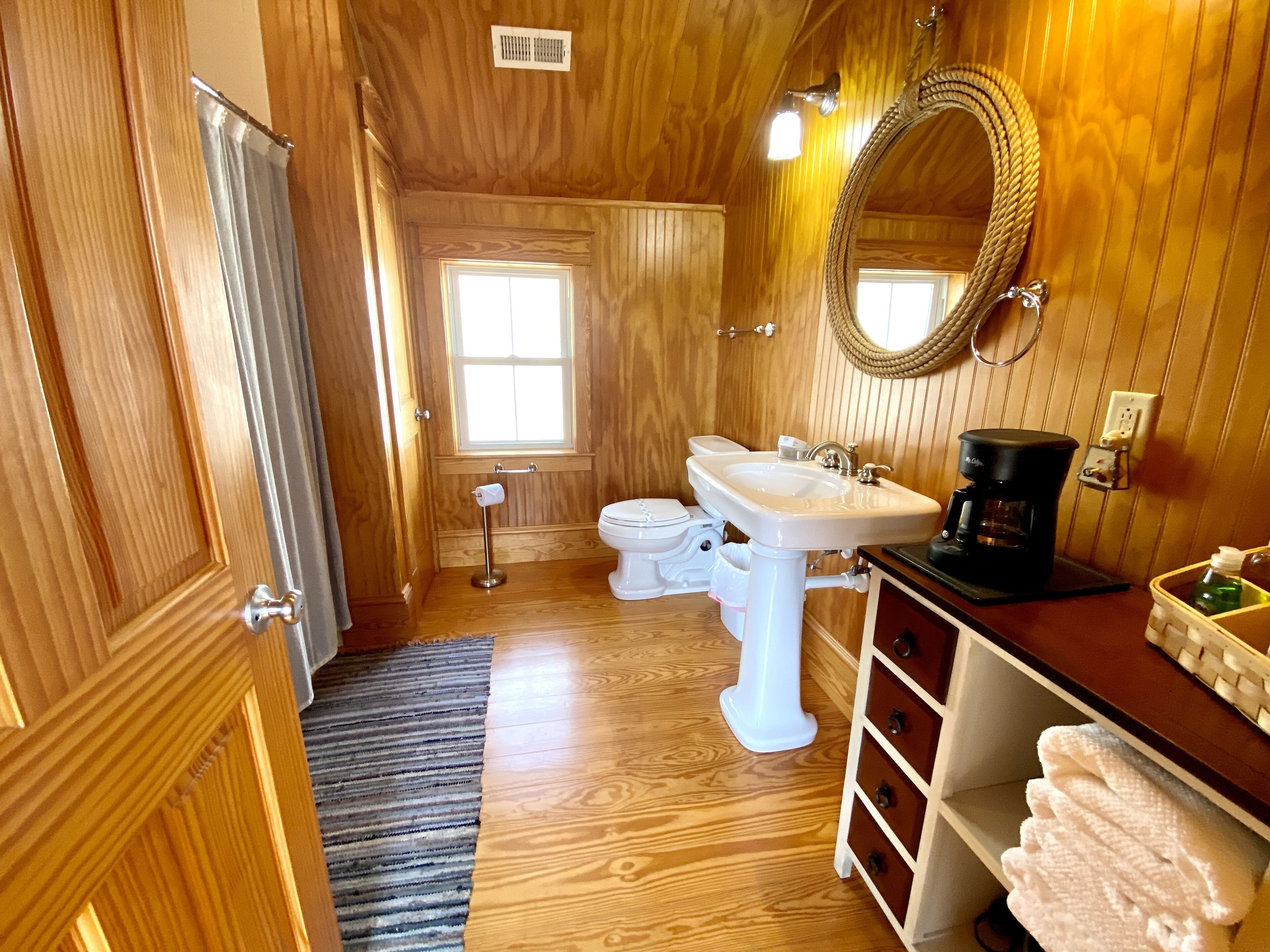 A wooden-paneled bathroom with a white pedestal sink, a toilet, and a large mirror.
