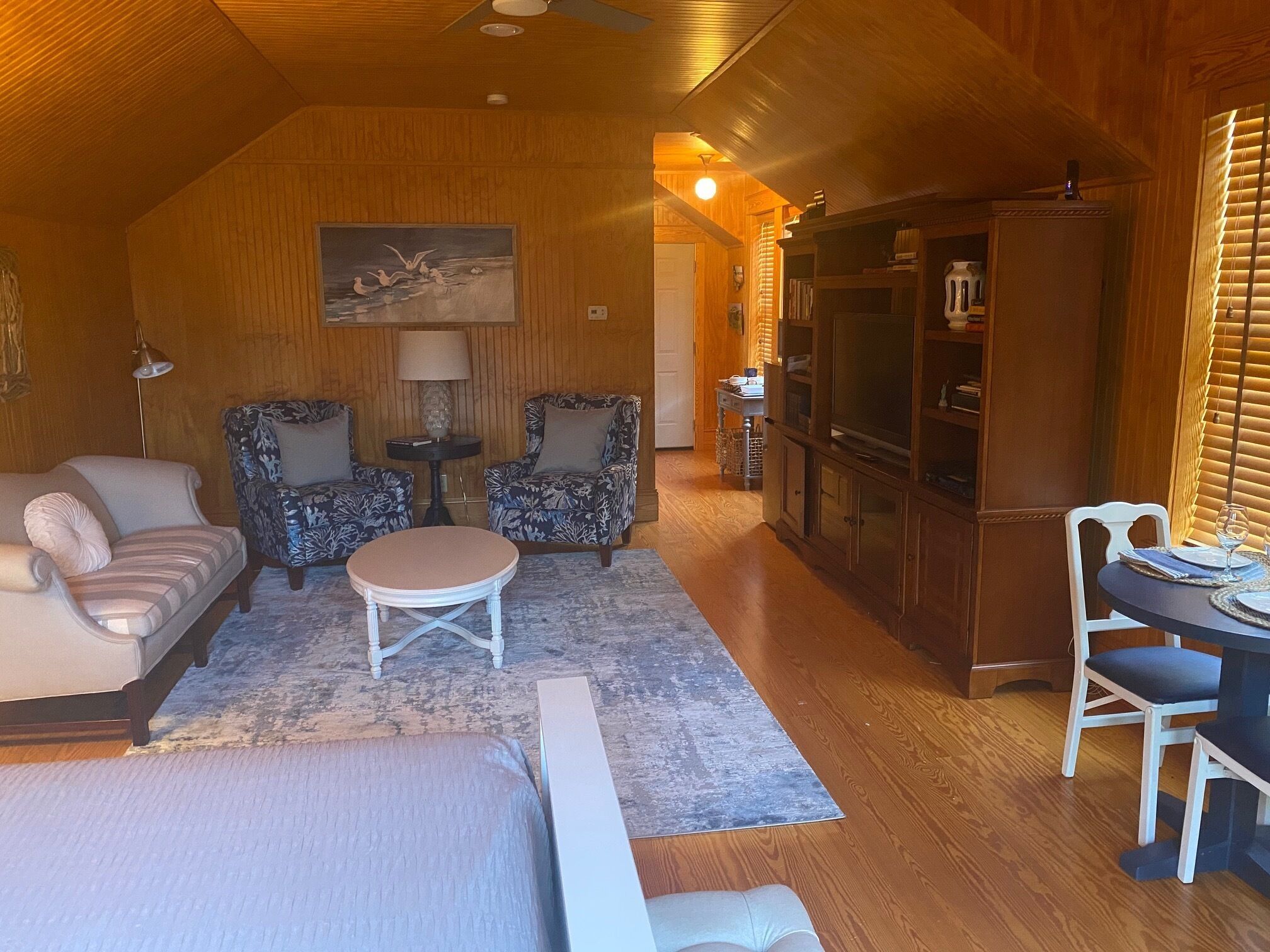 A cozy living room with a sofa, two patterned armchairs, a small round table, and a television set.