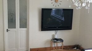 Un salon doté d’un téléviseur à écran plat fixé au mur, d’une petite table avec une lampe, d’une table basse en verre et d’un lustre.