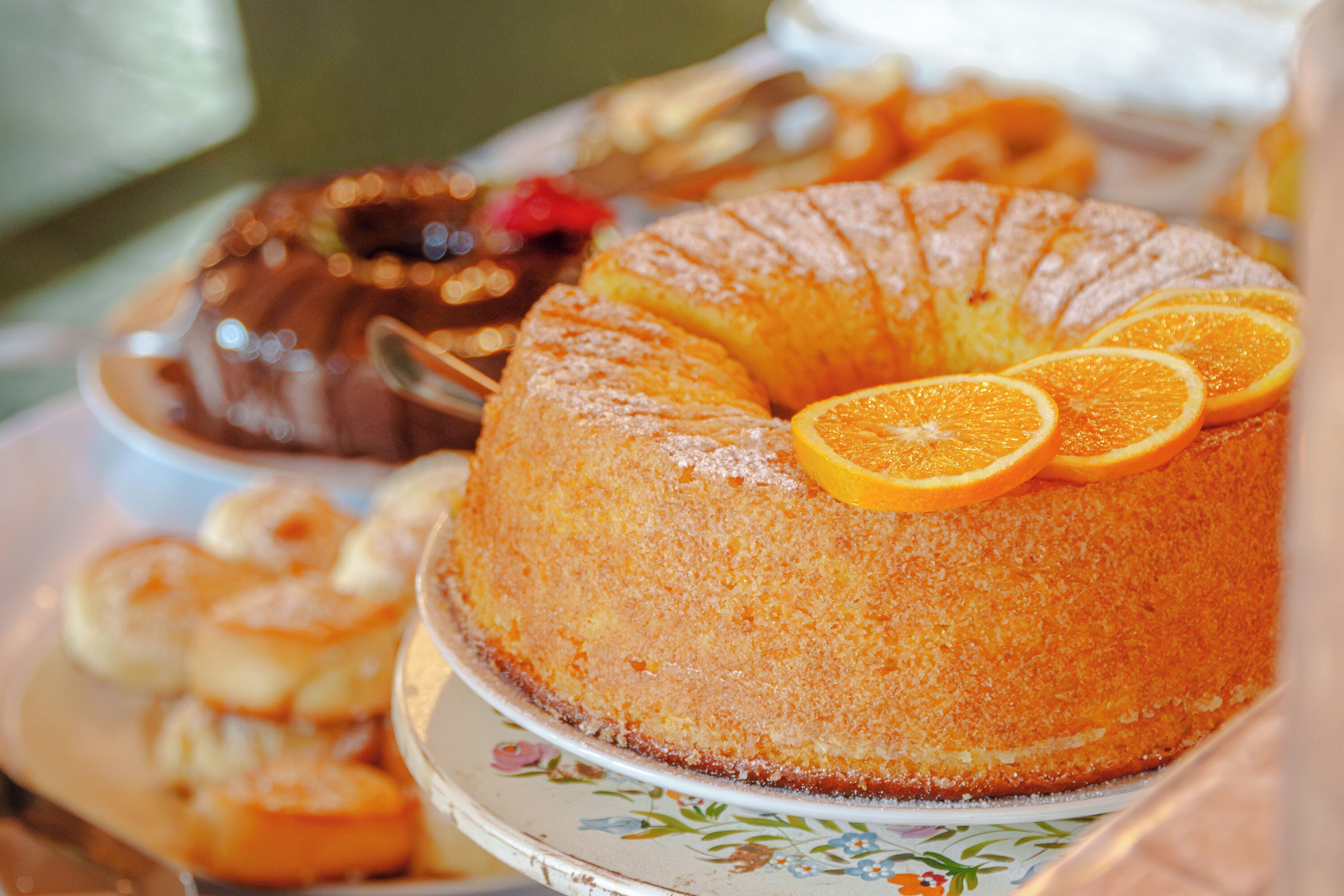 A cake with orange slices on top, surrounded by other desserts.
