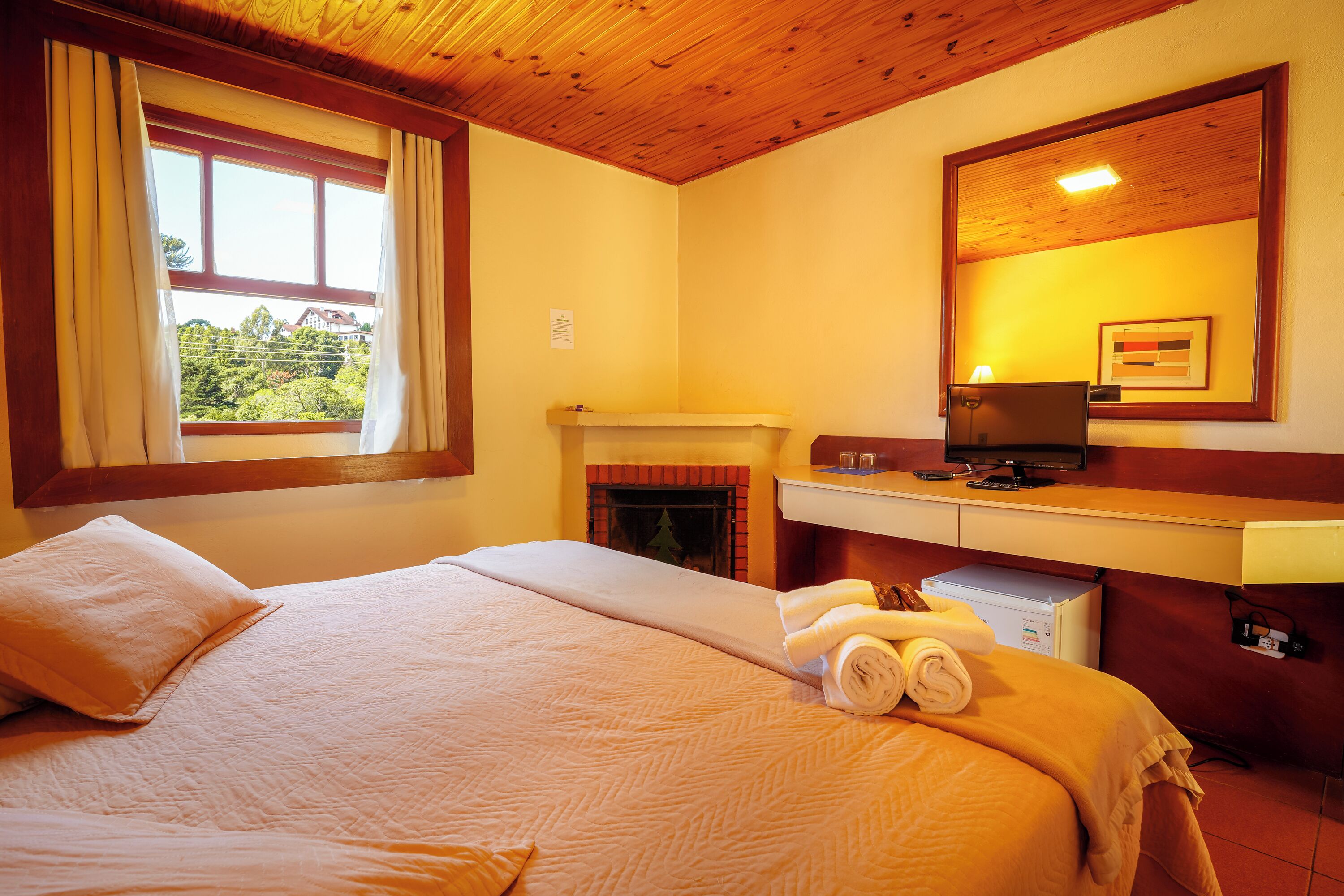 A hotel room with a bed, a fireplace, a desk with a computer, and a window with curtains.
