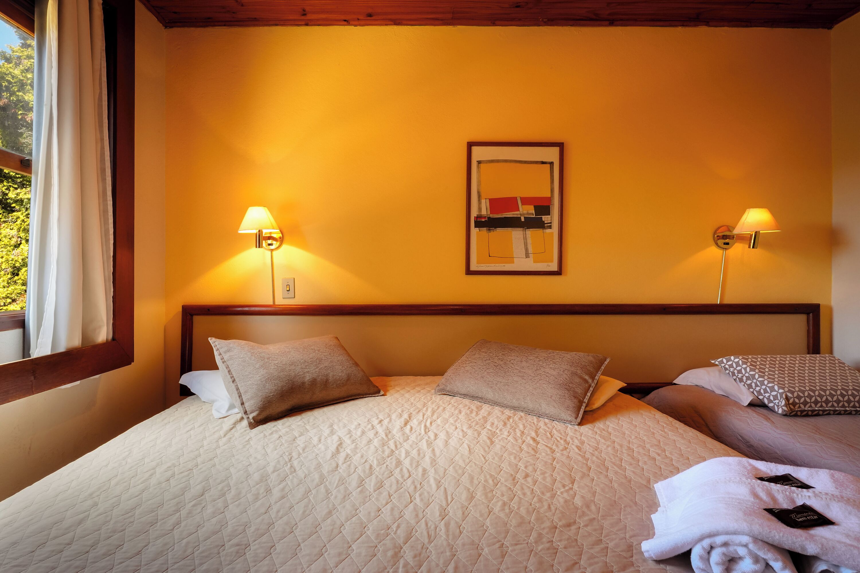 Una habitación de hotel con una cama grande, dos lámparas de noche, un cuadro en la pared y una ventana con cortinas.