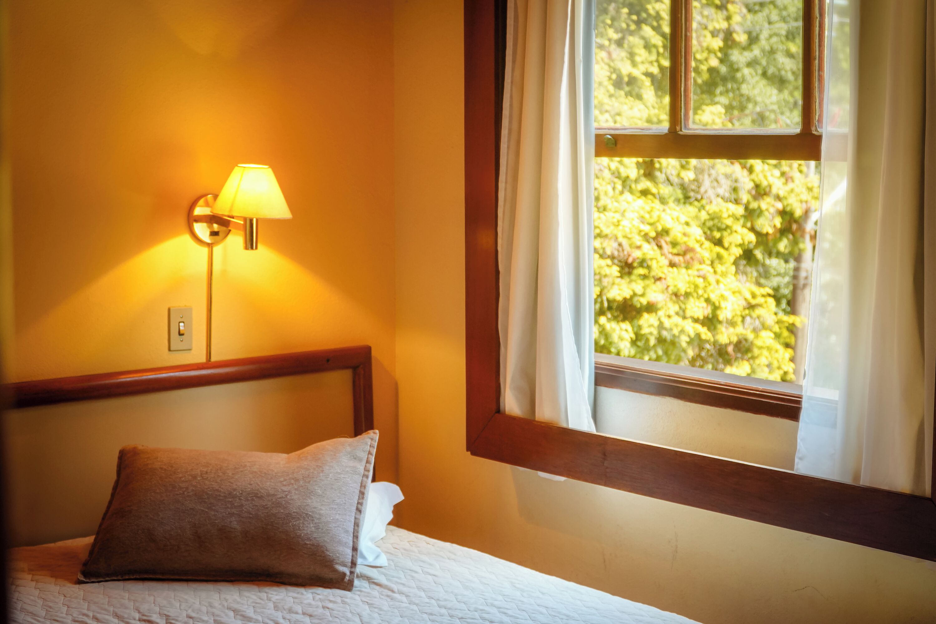 Ein Schlafzimmer mit einem Bett, einem Nachttisch, einer Lampe und einem Fenster mit Vorhängen.