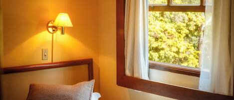 Ein Schlafzimmer mit einem Bett, einem Nachttisch, einer Lampe und einem Fenster mit Vorhängen.