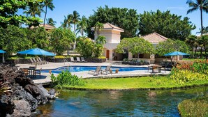 A pool area with lounge chairs and umbrellas, surrounded by tropical vegetation and a small water feature.