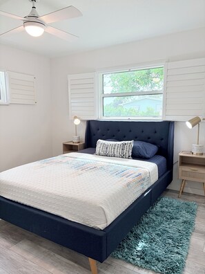 A bedroom with a bed, a ceiling fan, a window, and two bedside tables.