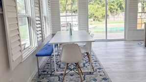 Une pièce spacieuse avec une grande table et des chaises, un banc bleu et une vue sur une cour arrière avec une piscine.