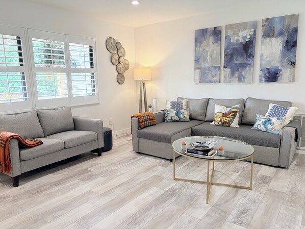 A modern living room with two grey sofas, a glass coffee table, and abstract wall art.