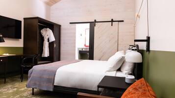 A hotel room with a bed, a desk, a chair, a TV, and a wardrobe.