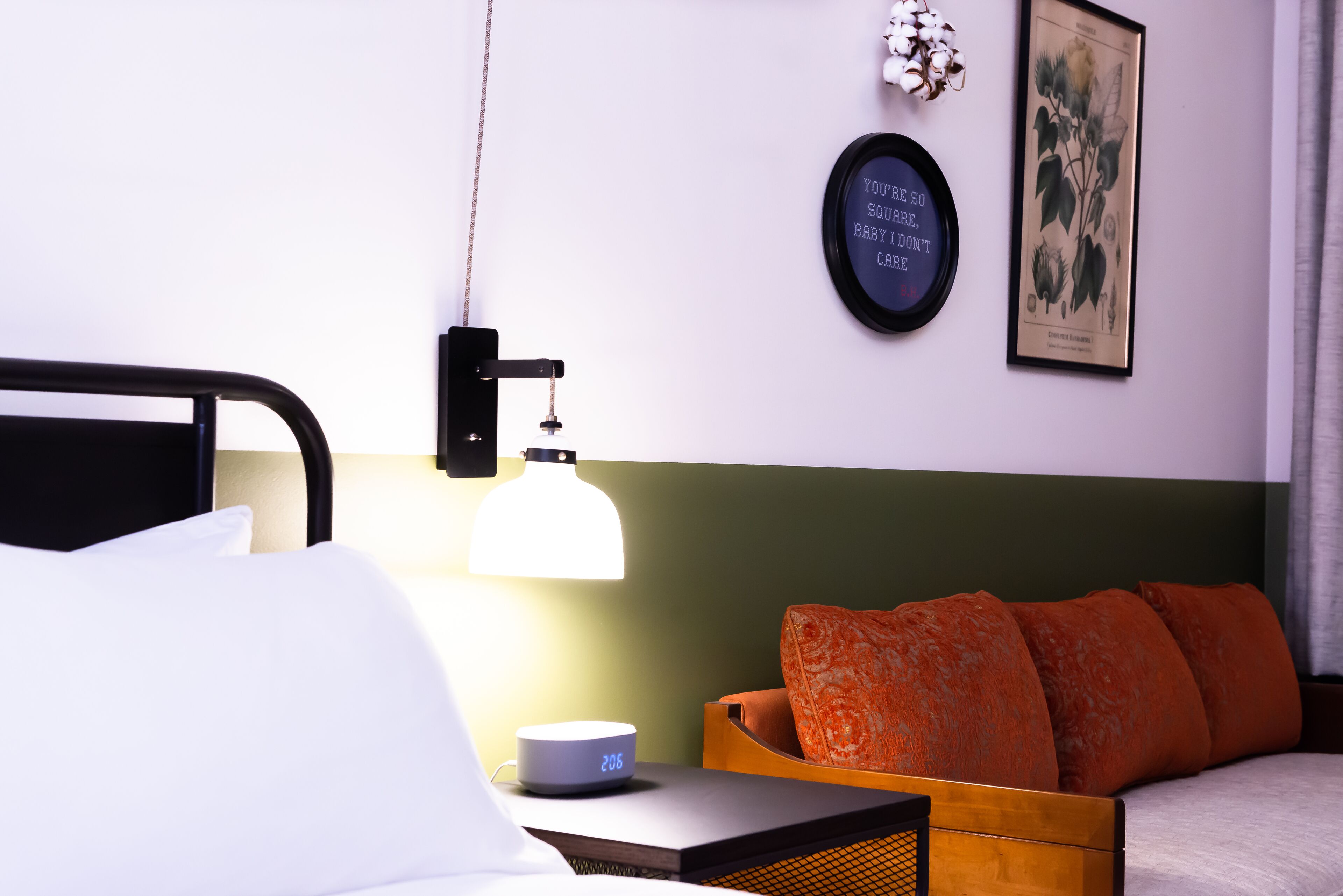 A neatly made bed with white linens, a bedside table with a lamp, a clock, and a framed quote on the wall.
