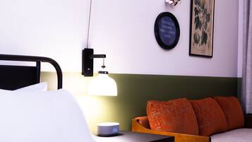 A neatly made bed with white linens, a bedside table with a lamp, a clock, and a framed quote on the wall.