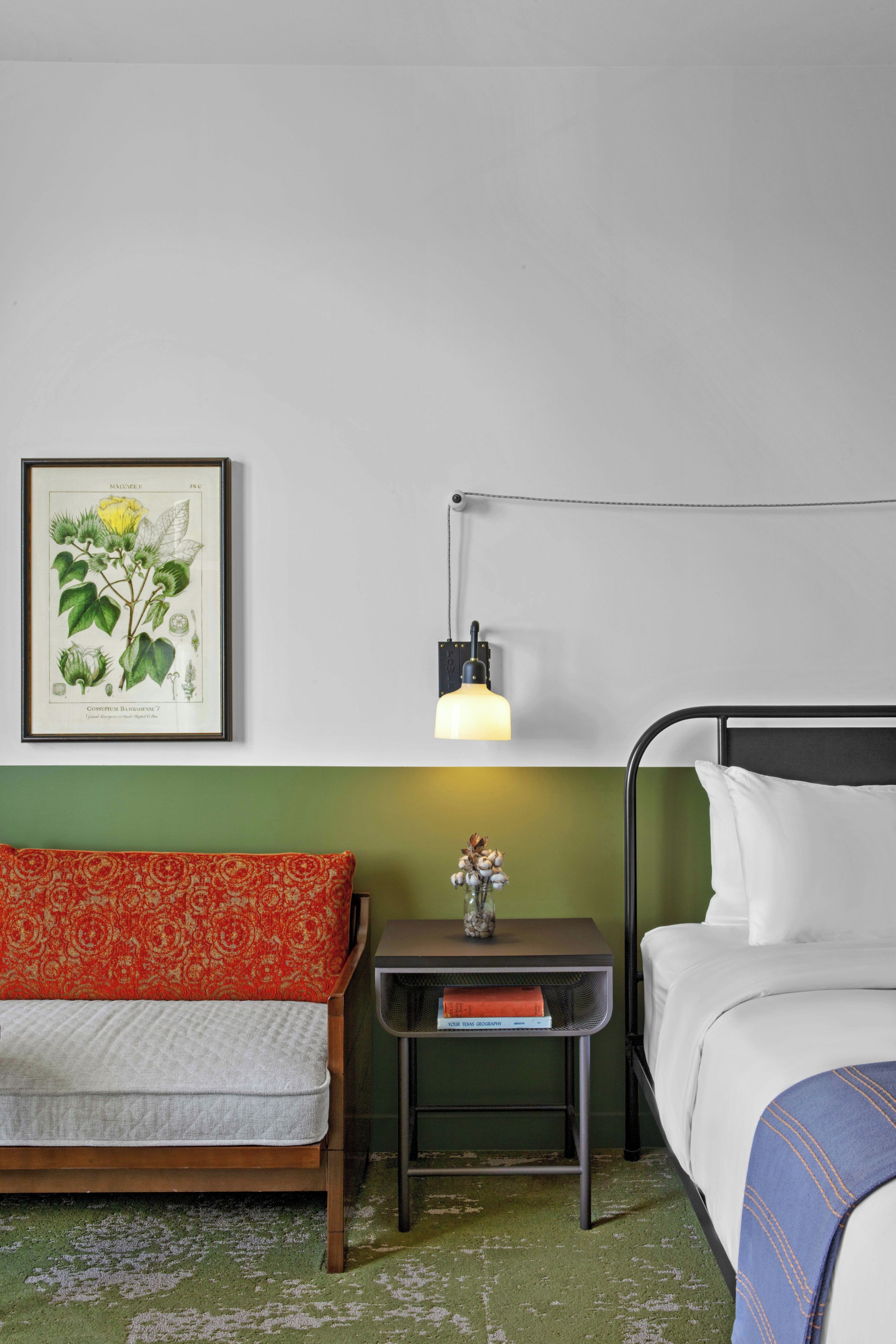 A room with a bed, a nightstand, a lamp, a framed botanical illustration, and a patterned sofa.