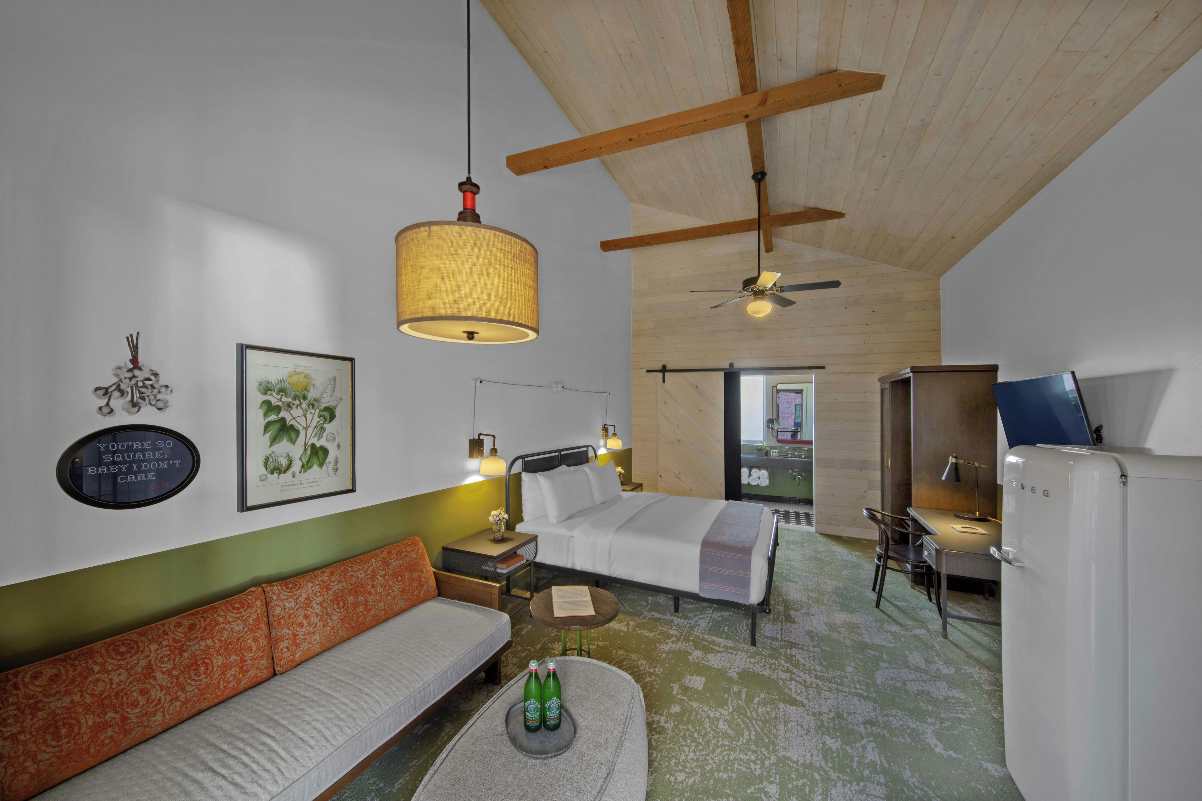 A hotel room with a bed, a sofa, a desk, and a kitchenette.
