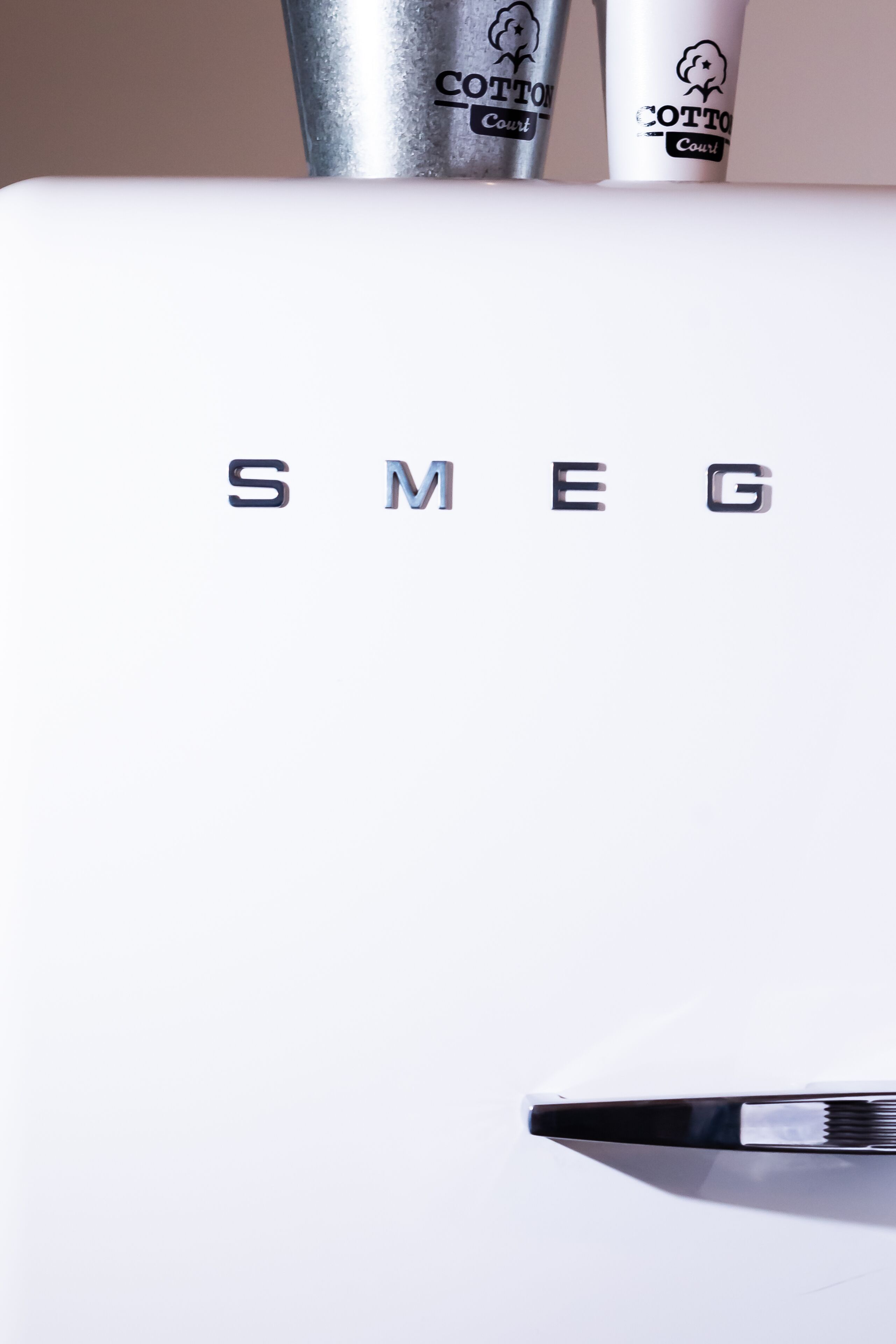 A white surface with the text "SMEG" and two cotton-themed containers.