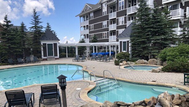 A pool area with lounge chairs, a covered seating area, and a multi-story building with balconies. - Allegheny Springs Slope Side Penthouse - Amazing Views (Snowshoe)
