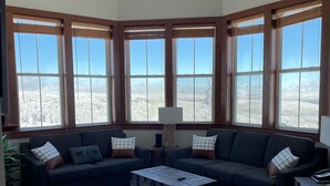 A corner living room with a sectional sofa, a coffee table, and large windows with a snowy view. - Allegheny Springs Slope Side Penthouse - Amazing Views (Snowshoe)