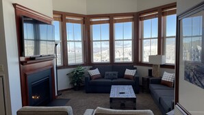 A cozy living room with a fireplace, large windows, and a view of a snowy landscape. - Allegheny Springs Slope Side Penthouse - Amazing Views (Snowshoe)