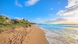 A beach with footprints, a building with balconies, and a clear sky.