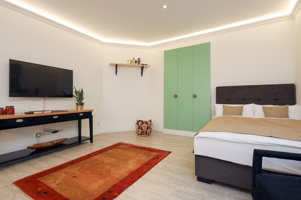 A modern bedroom with a bed, a TV, a desk, a green wardrobe, and a red rug.