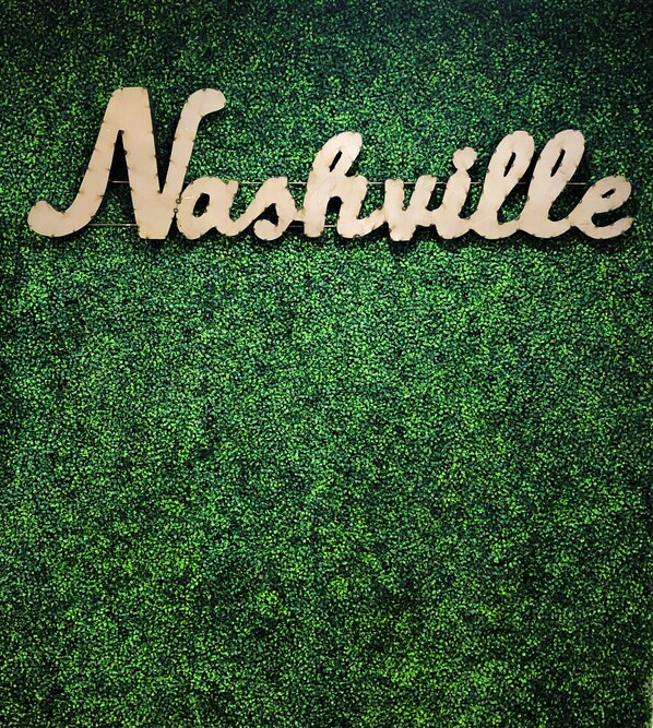 Une enseigne en bois sur laquelle on peut lire le mot « Nashville », le tout sur un fond vert à texture.