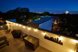 Une terrasse sur le toit offrant une vue panoramique sur la ville, avec des sièges en plein air et des guirlandes lumineuses.