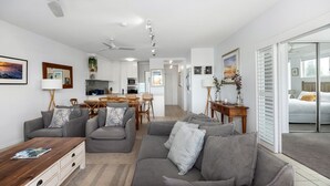 A modern living room with grey sofas, a wooden coffee table, and a kitchen in the background. - Sempre 7 Sunshine Beach (Sunshine Beach)