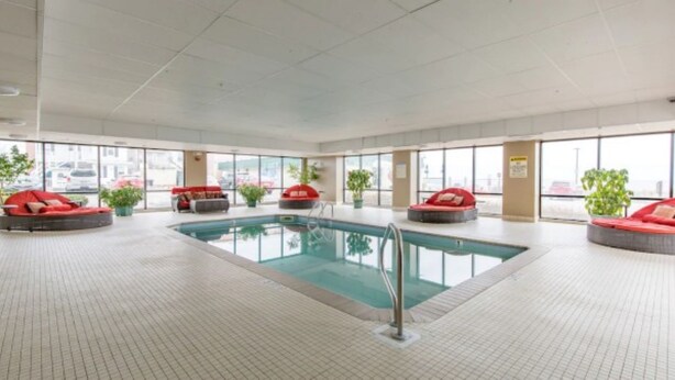 Una amplia piscina cubierta con varias zonas de estar rojas y grandes ventanales.