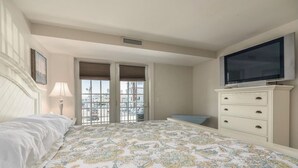 Un dormitorio con cama, cómoda, televisor y ventana con persianas.