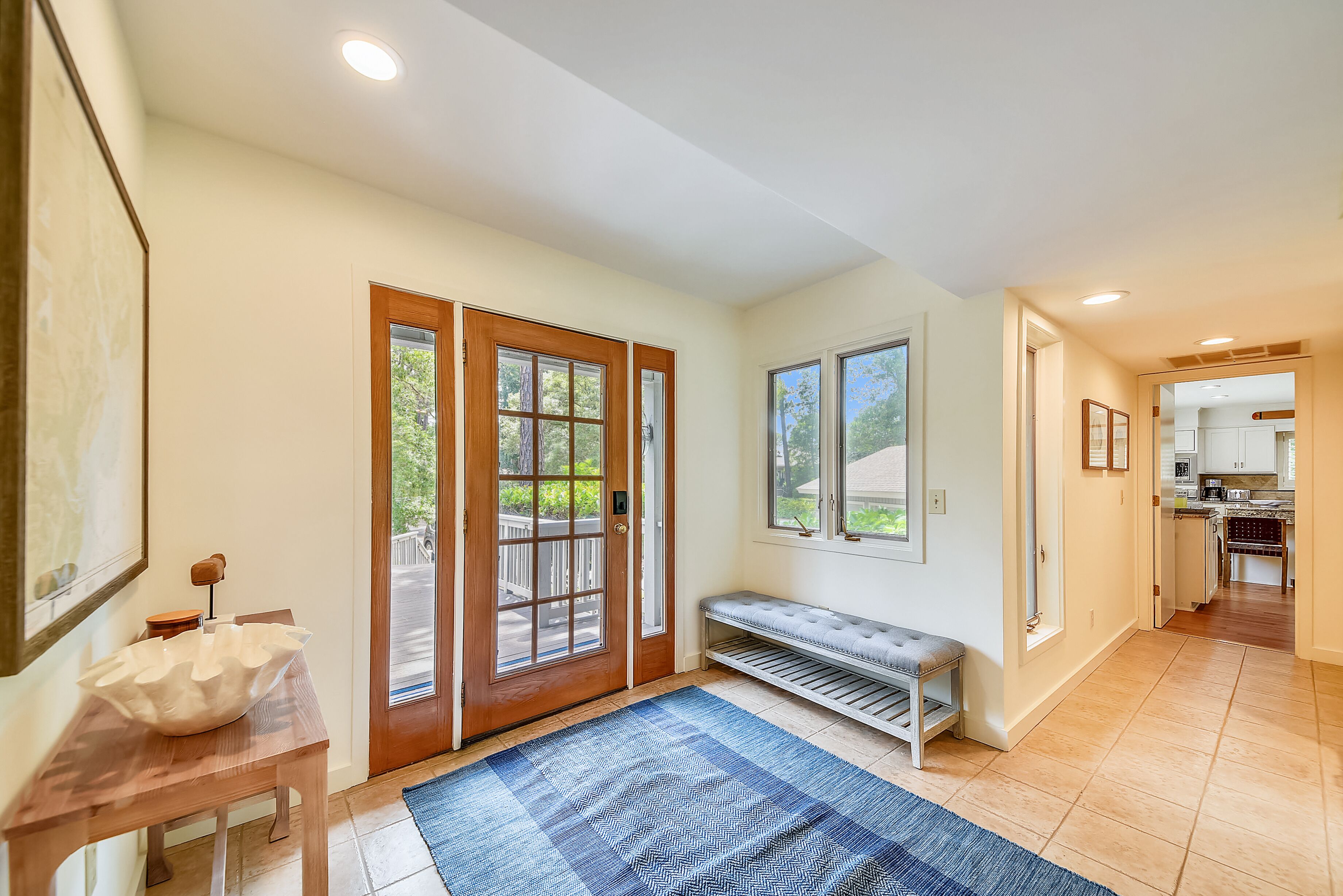 A spacious entryway with a bench, a large white bowl on a wooden table, and a view into the kitchen.